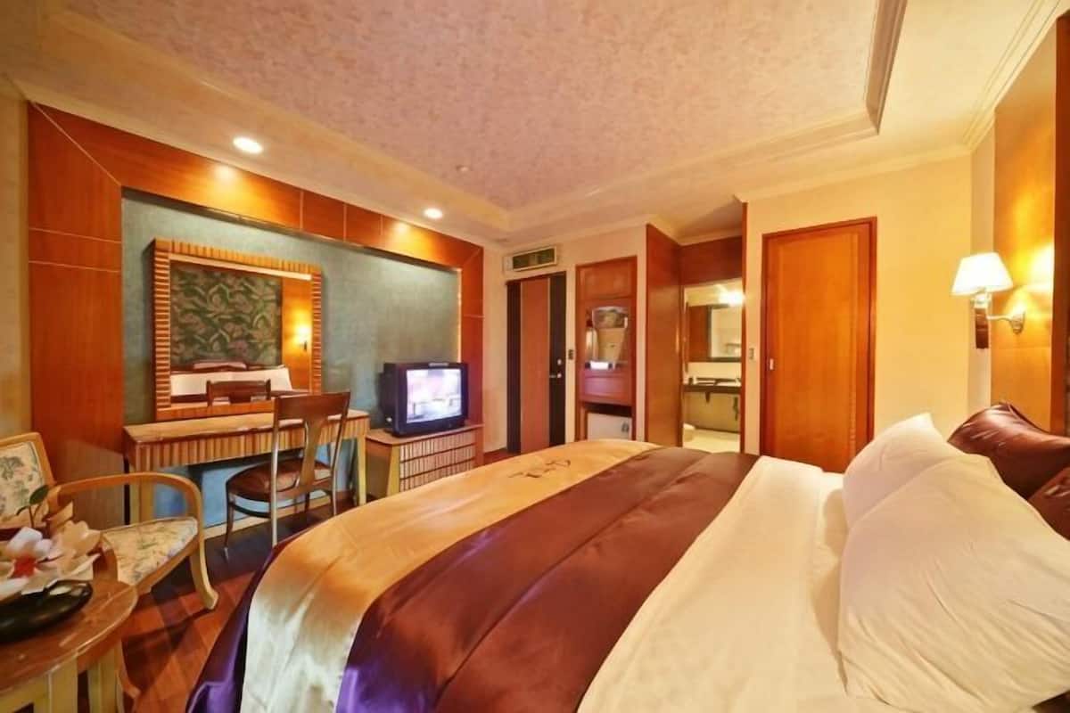 A hotel room with a bed, desk, television, and a bathroom door.