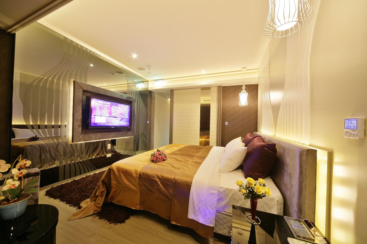 A modern hotel room with a large bed, a television, a desk with a phone, and a vase with flowers.