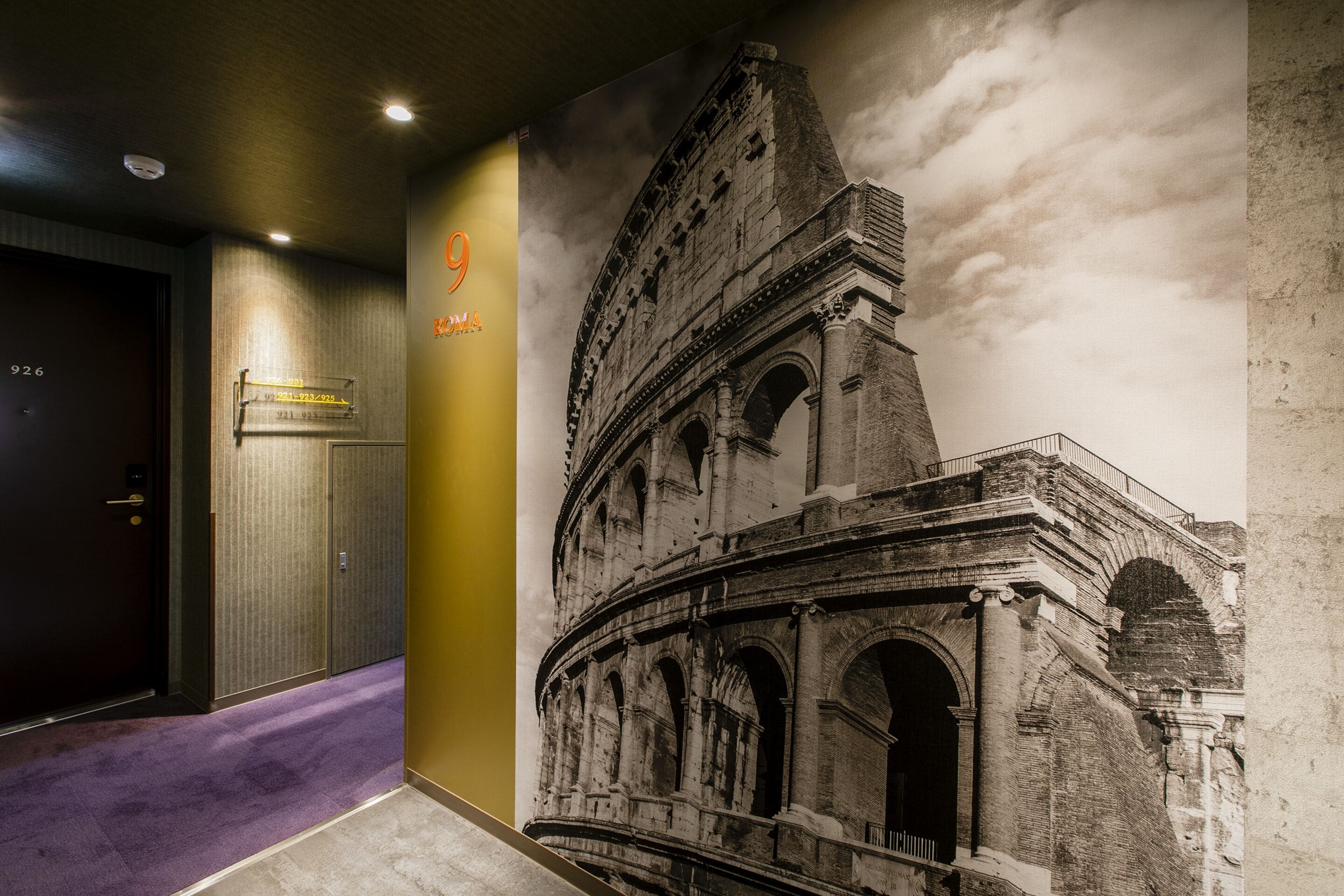 A hallway with a purple carpet, a door labeled "926", and a large mural of the Colosseum.