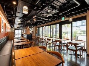 L’intérieur d’un restaurant, avec des tables et des chaises en bois, un espace cuisine et de grandes fenêtres donnant sur l’extérieur.