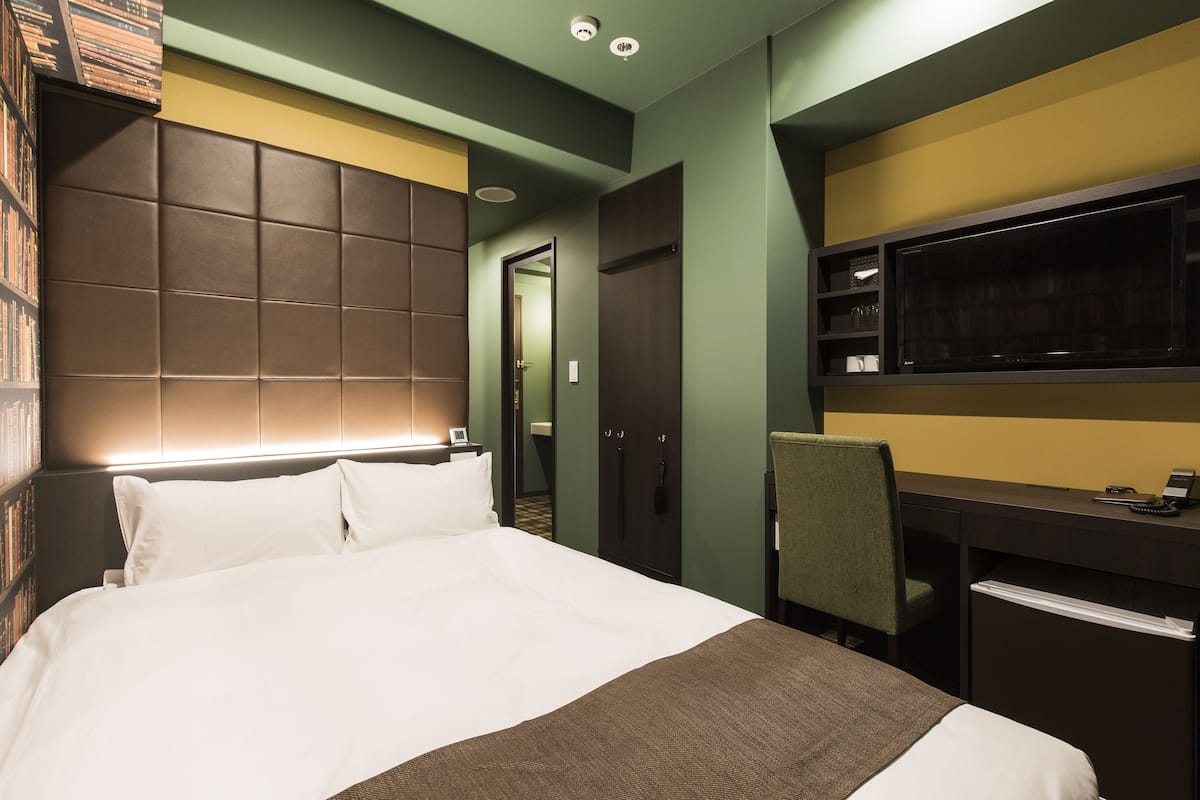 Una habitación de hotel con una cama grande, un escritorio con silla, un televisor y un armario.
