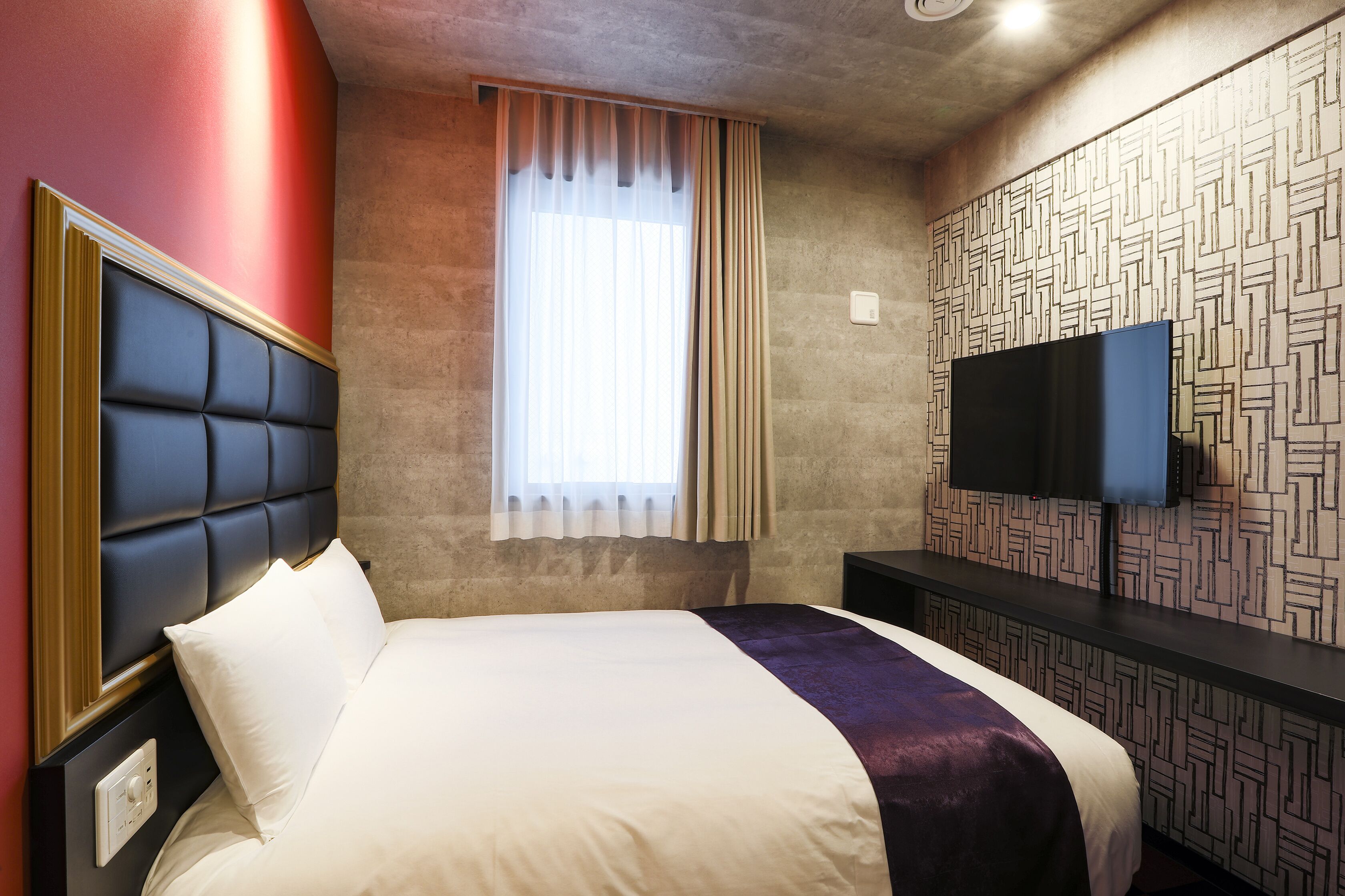 A hotel room with a large bed, a TV mounted on the wall, and a window with curtains.
