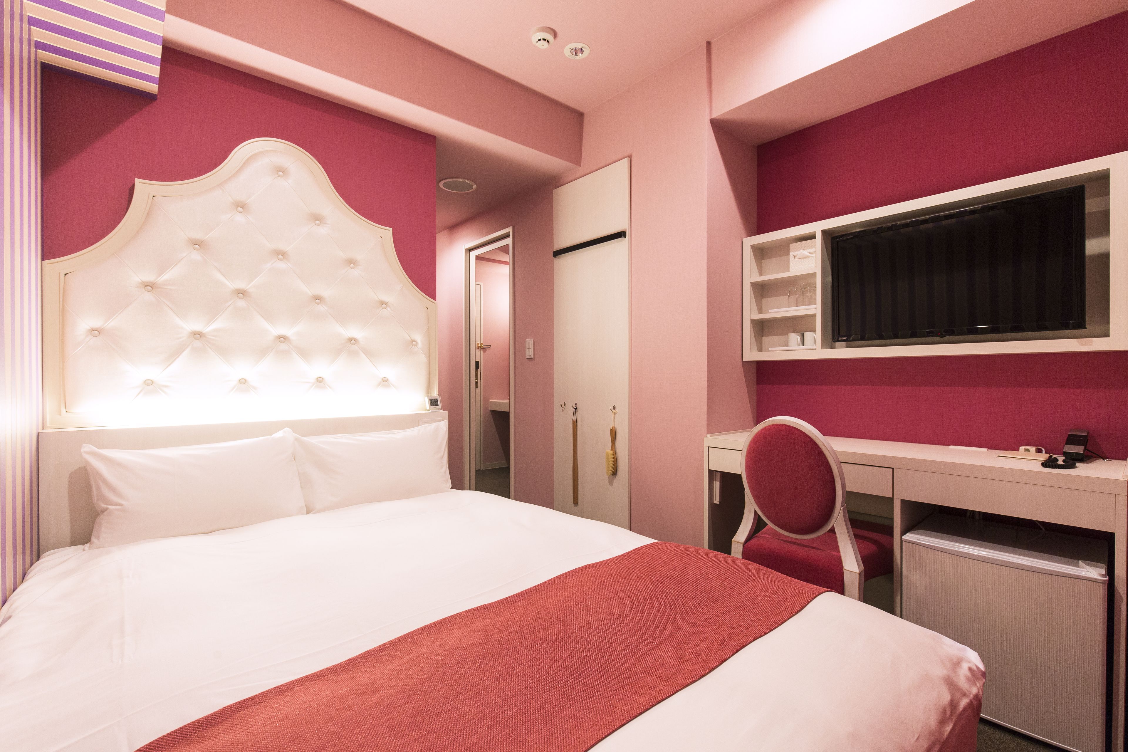 Una habitación de hotel con una cama grande, un escritorio con silla, un televisor y un armario.