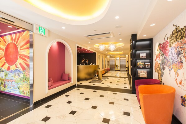 Un vestíbulo de hotel con una recepción, zonas de estar y un mural decorativo.