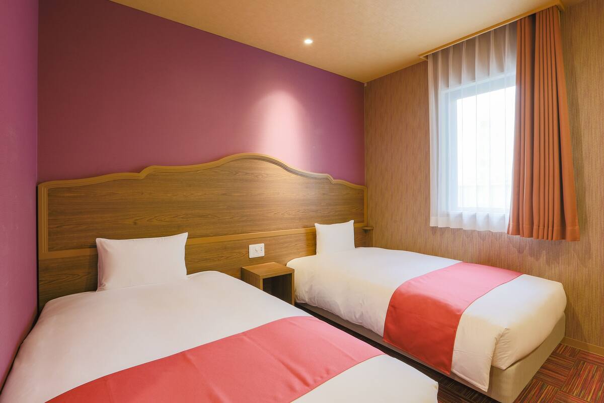 Habitación de hotel con dos camas, cabeceros de madera y una ventana con cortinas.