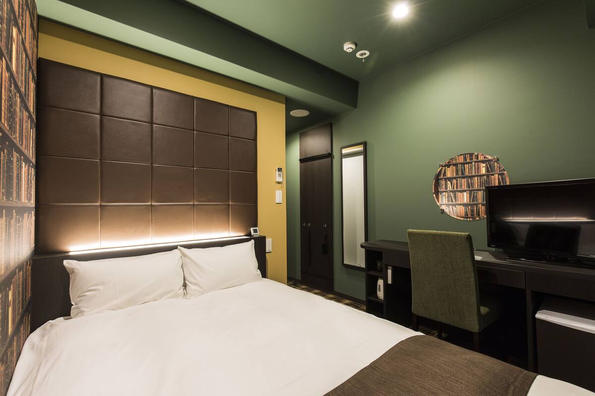 Una habitación de hotel con una cama grande, un escritorio con una silla, un televisor y una estantería.