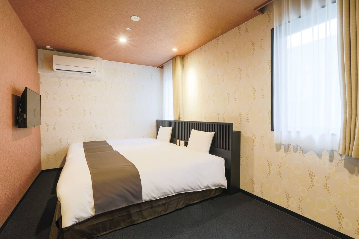 Habitación de hotel con cama, aire acondicionado, televisor y ventana con cortinas.