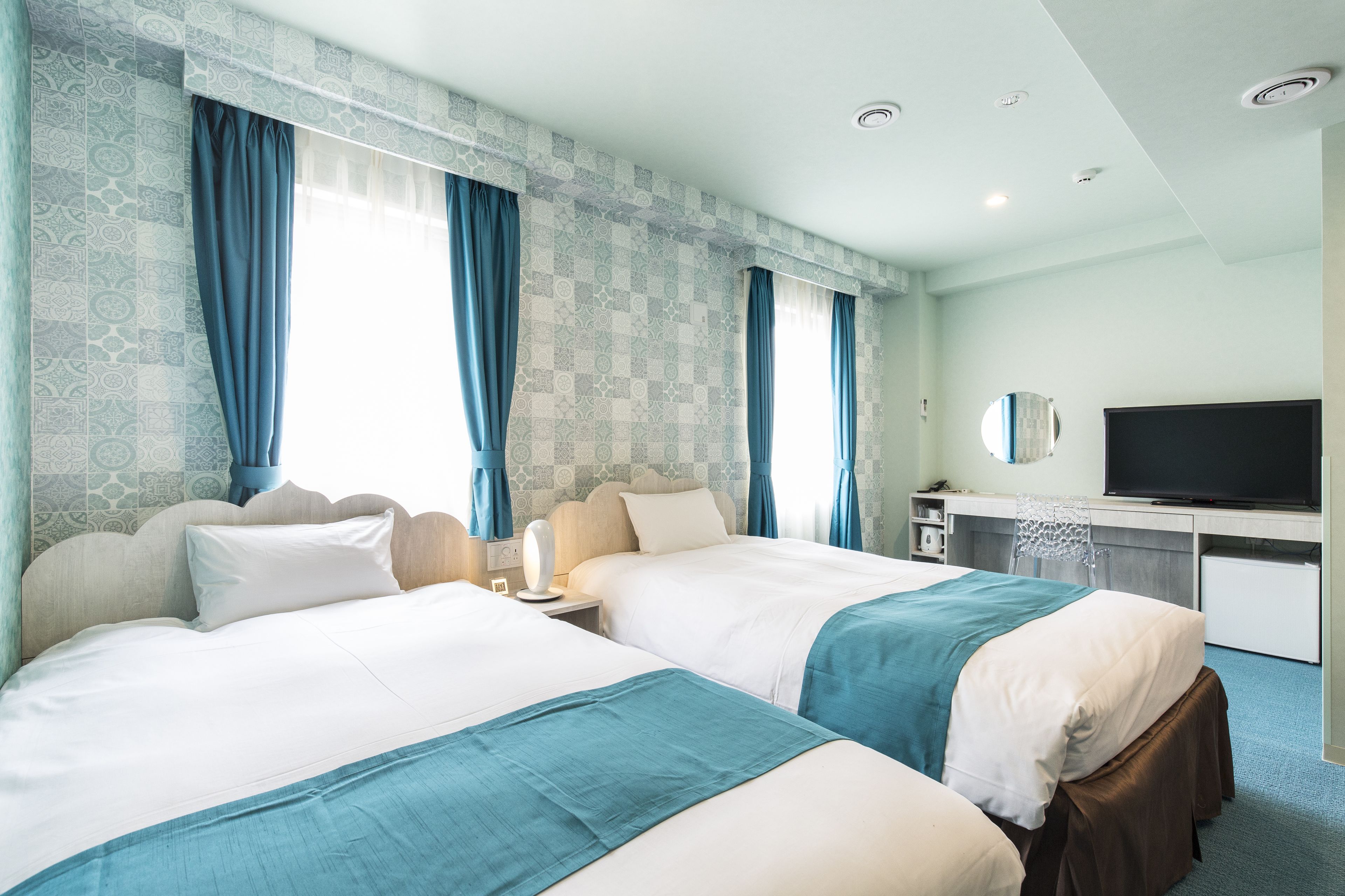 Ein Hotelzimmer mit zwei Betten, einem Fernseher, einem Schreibtisch und einem Fenster mit Vorhängen.