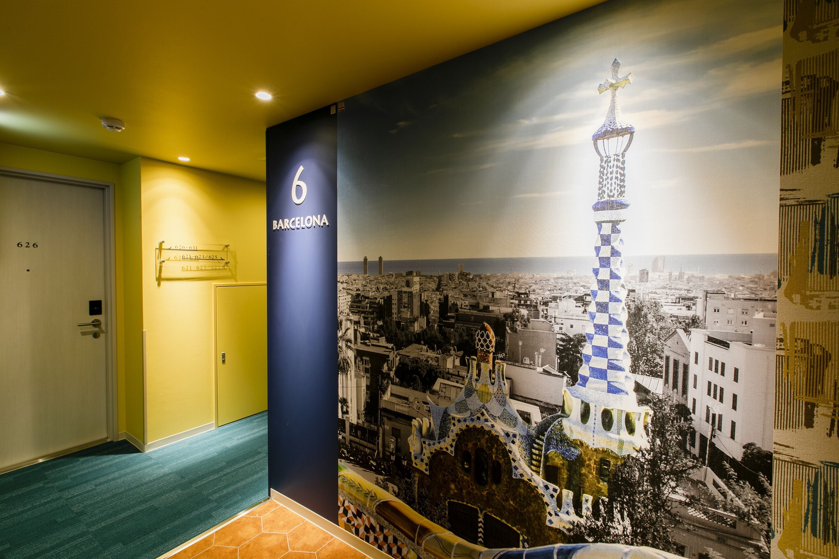 A hallway with a large poster of a famous tower, a door with a number, and a carpeted floor.