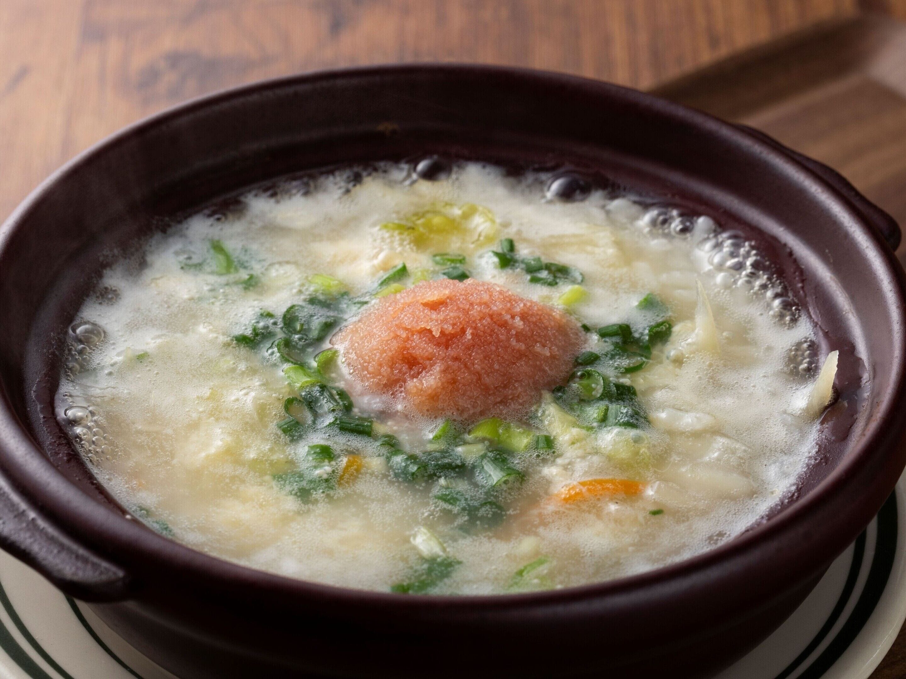 Un tazón de sopa con un objeto redondo y rosado en el centro, rodeado de hierbas y verduras verdes.
