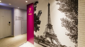 A hallway with a large mural of the Eiffel Tower, a door labeled "7 PARIS", and a sign indicating room numbers.
