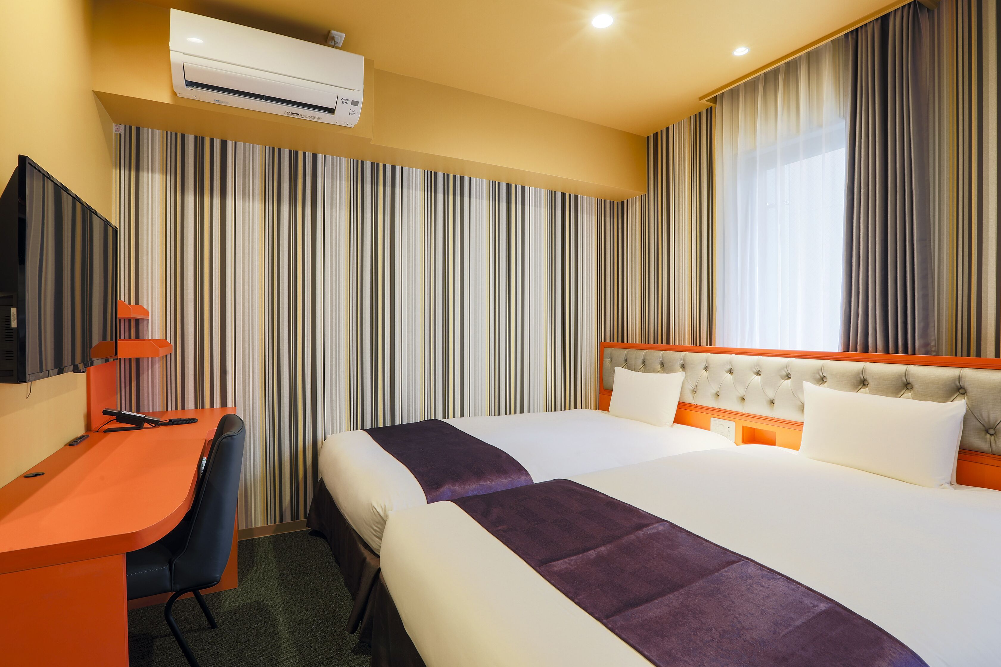 A hotel room with two beds, a desk, a chair, and a TV.