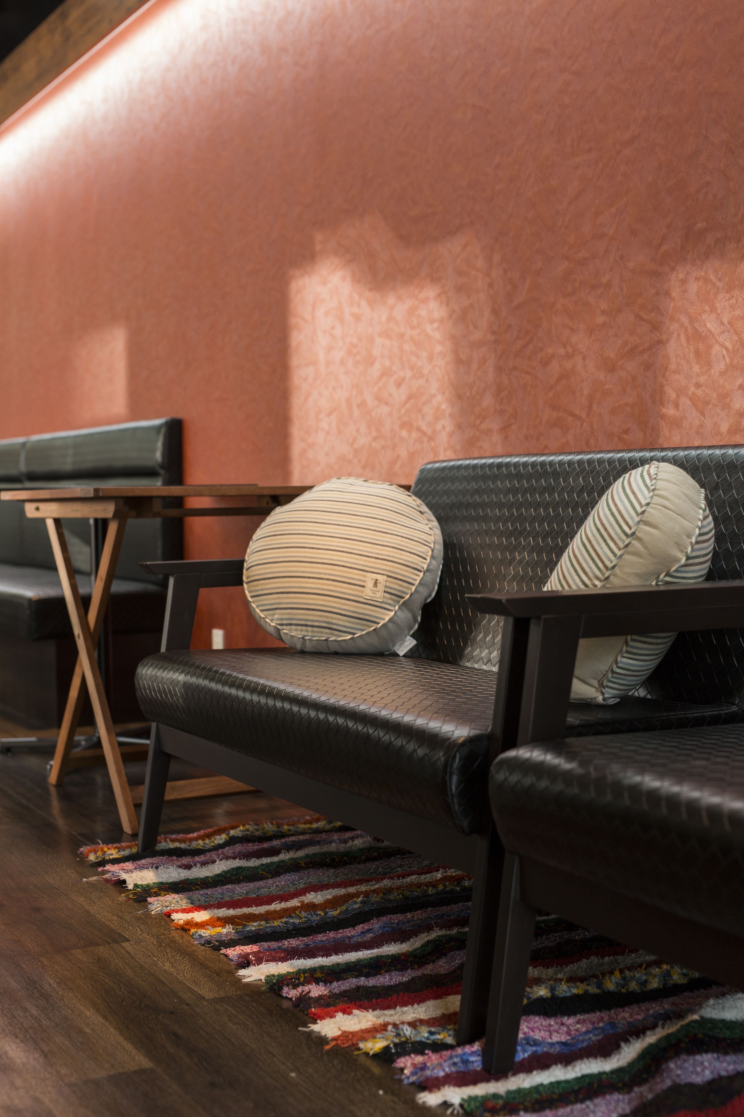 Un sofá de cuero negro con almohadones a rayas, una mesa de madera y una alfombra colorida con diseño a rayas sobre un piso de madera.