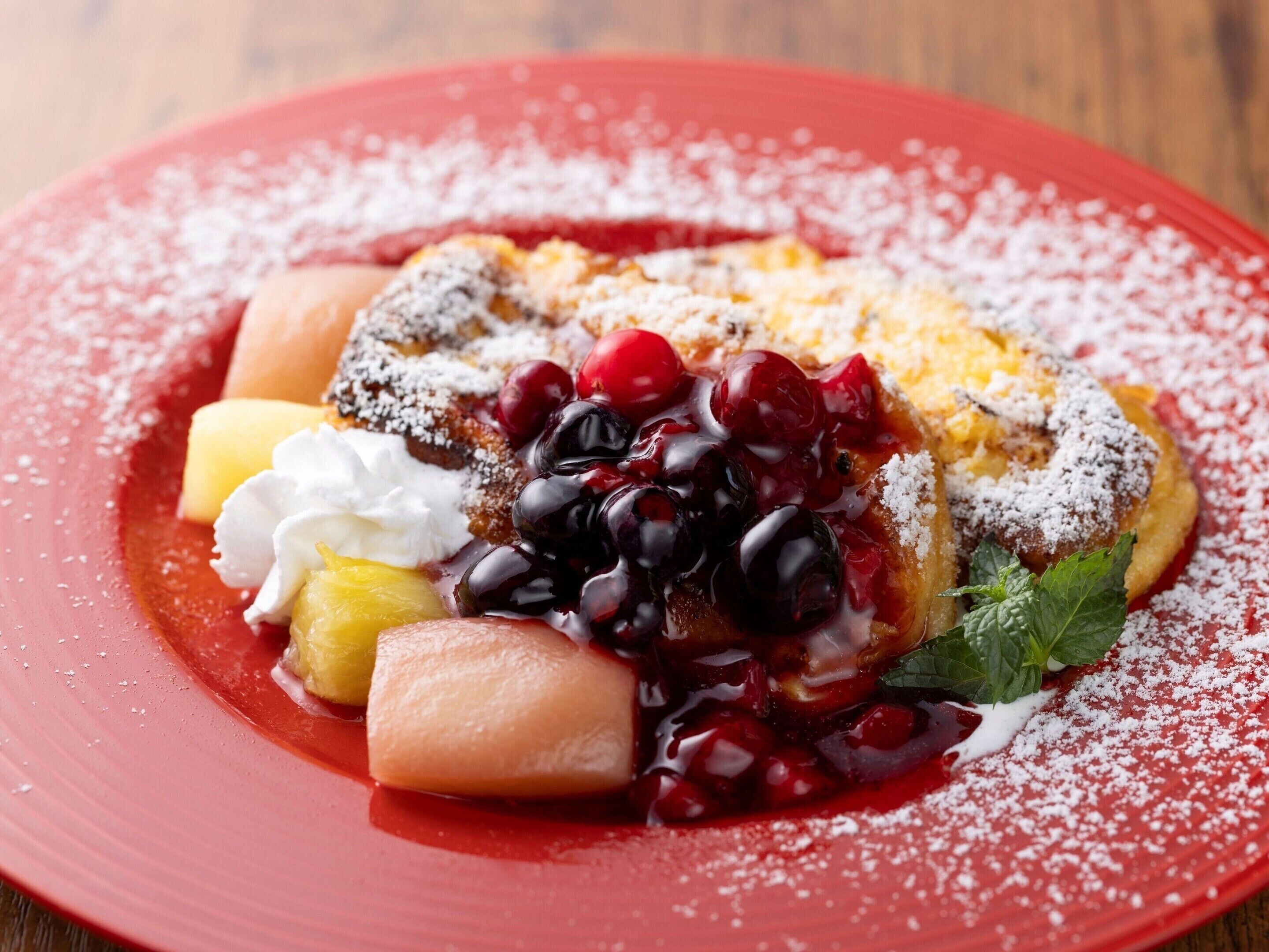A dessert plate with a slice of cake, whipped cream, cherries, and a mint leaf.