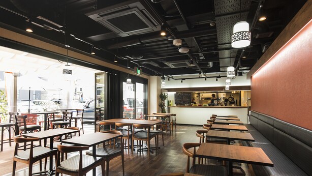 A restaurant interior with wooden tables and chairs, a counter with a menu, and a view of the street outside.