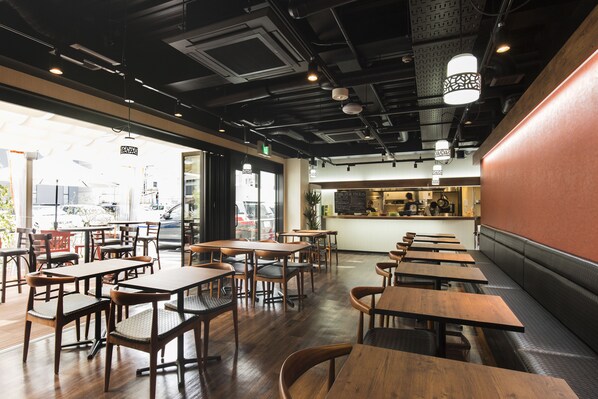 Interior de restaurante con mesas y sillas de madera, una barra con menú y vista a la calle.