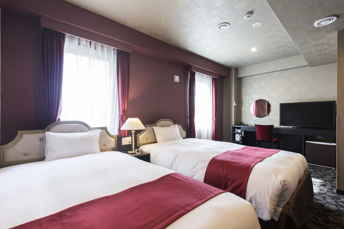 Habitación de hotel con dos camas, un escritorio, un televisor y un espejo.