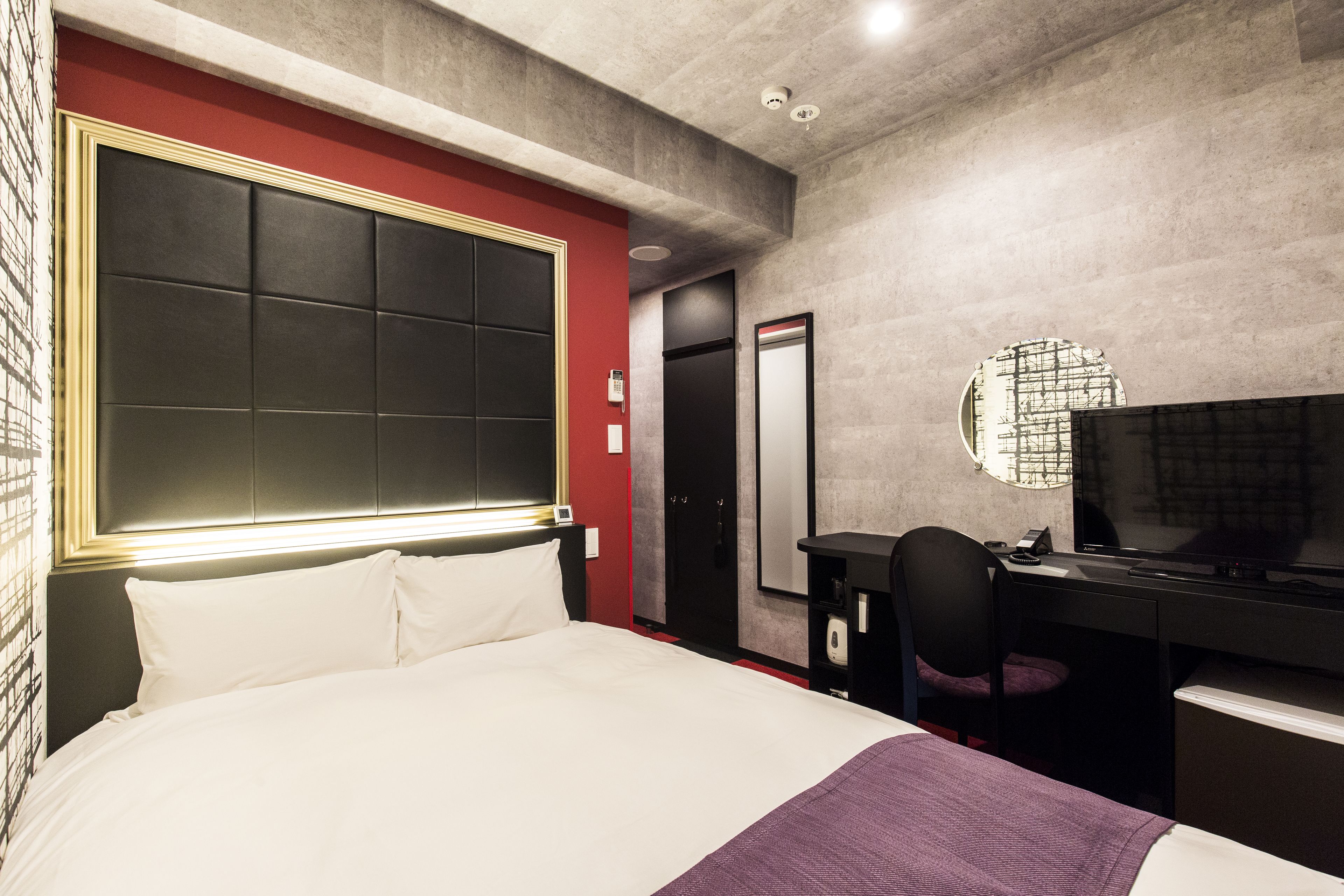 A hotel room with a large bed, a desk with a chair, a television, and a mirror.