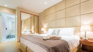 Ein modernes Hotelzimmer mit einem großen Bett, Nachttischlampen, einem Spiegel und einem hölzernen Kopfteil.