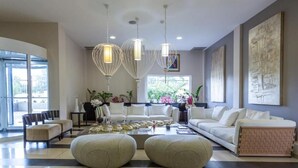 Ein großzügiges Wohnzimmer mit einer großen Sofagarnitur, einem Couchtisch und Pendelleuchten. Große Fenster sorgen für natürliches Licht und Blick ins Grüne.