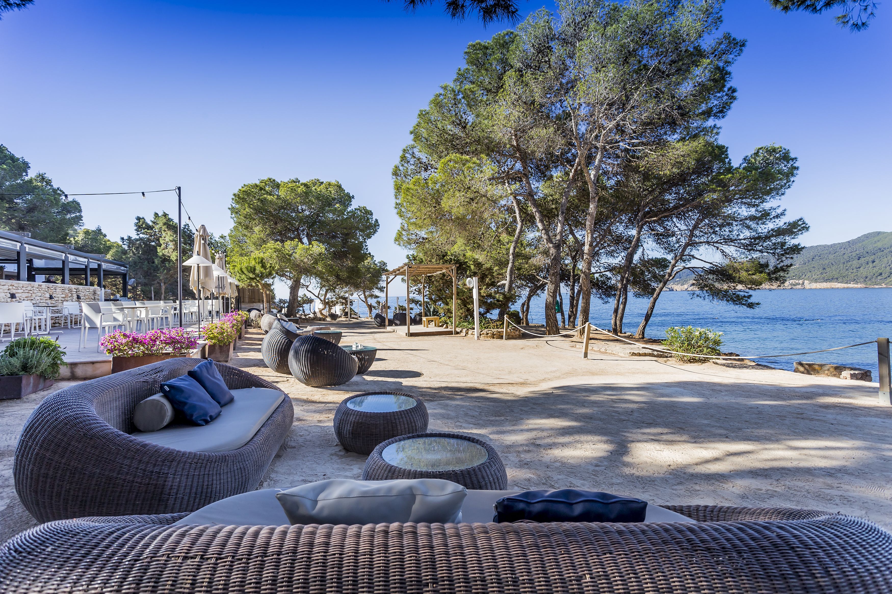 Un salón junto a la playa con mobiliario de mimbre, comedor al aire libre y vistas al mar.