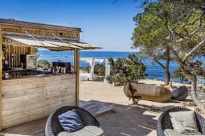 A wooden outdoor seating area with wicker chairs and a bar counter, overlooking a beach and the sea. - Catalonia Ses Estaques - Adults Only (Santa Eulalia del Rio)