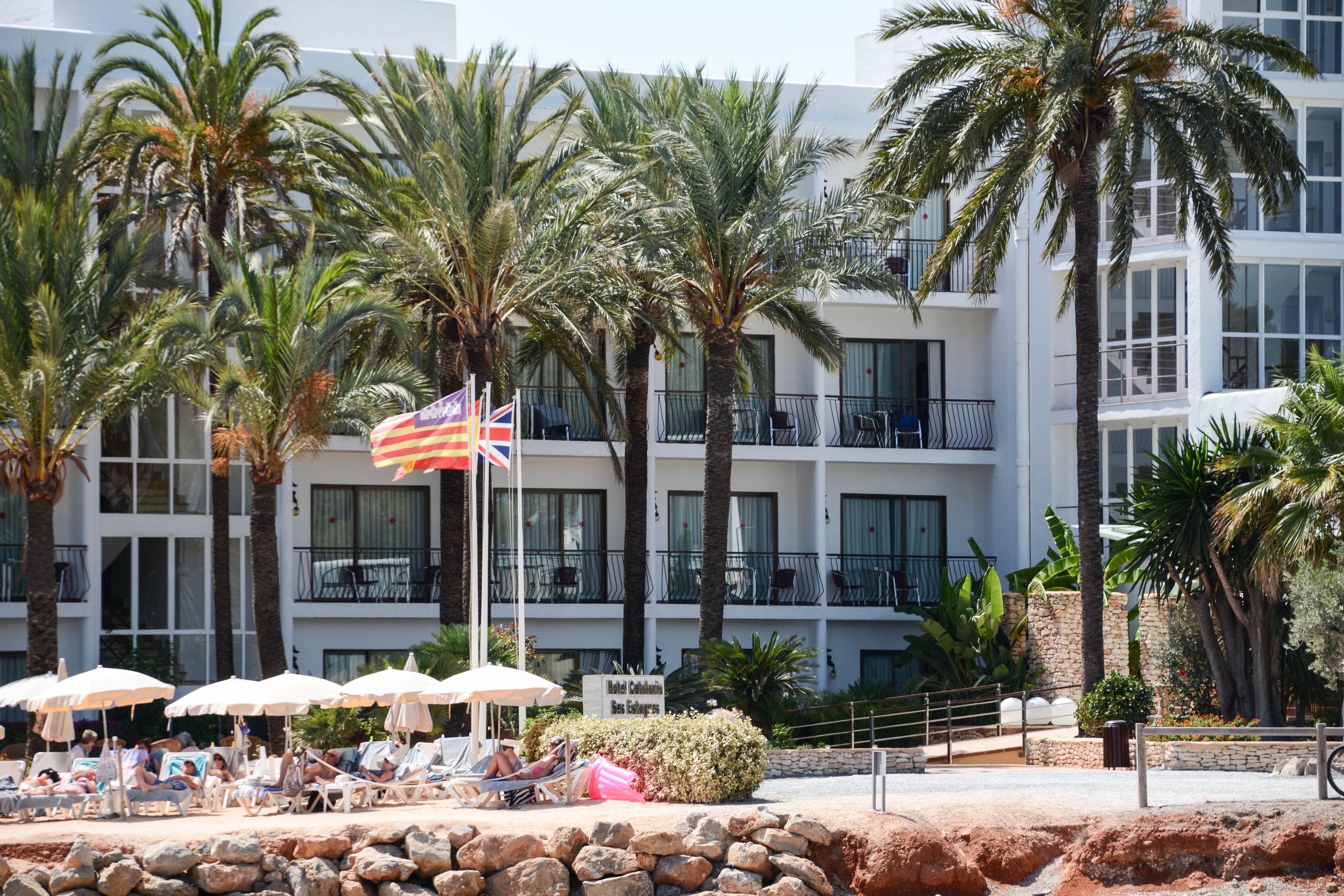 Un hotel con varios balcones, palmeras y sombrillas de playa.