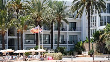 Un hotel con varios balcones, palmeras y sombrillas de playa.