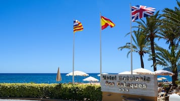 Señal de hotel con banderas, palmeras y sombrillas de playa.
