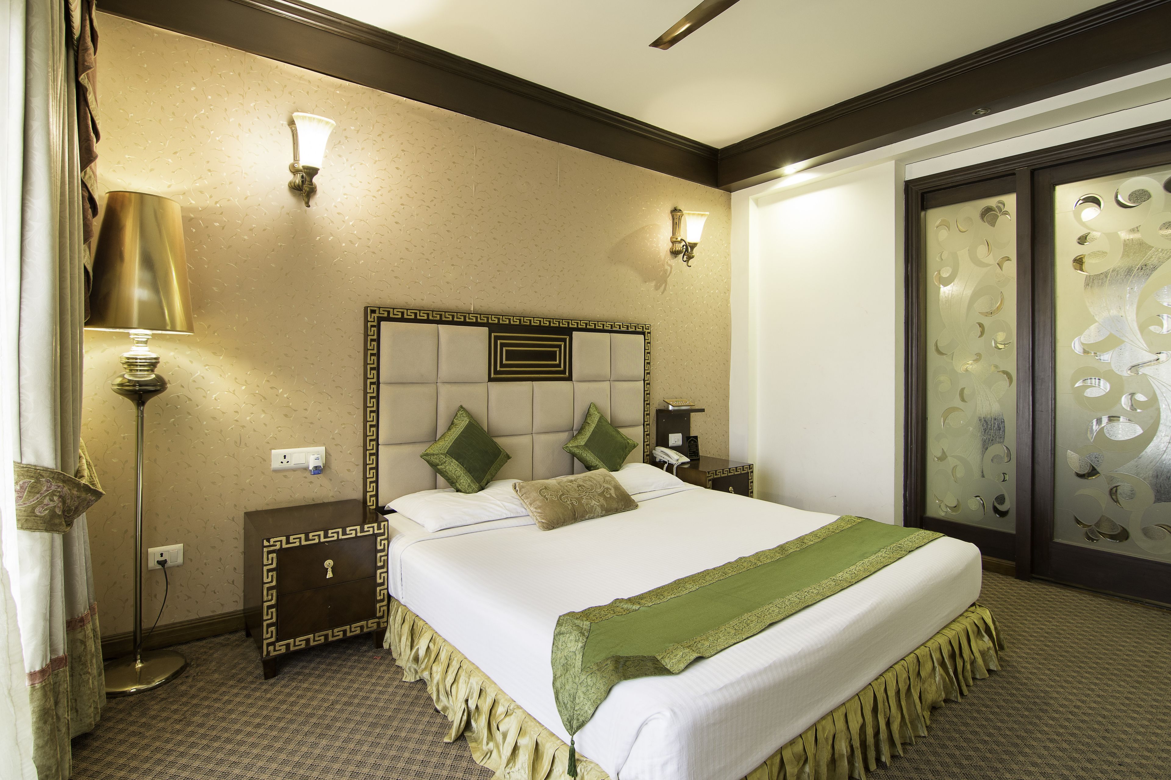 A hotel room with a large bed, a nightstand, a lamp, and a decorative wall panel.