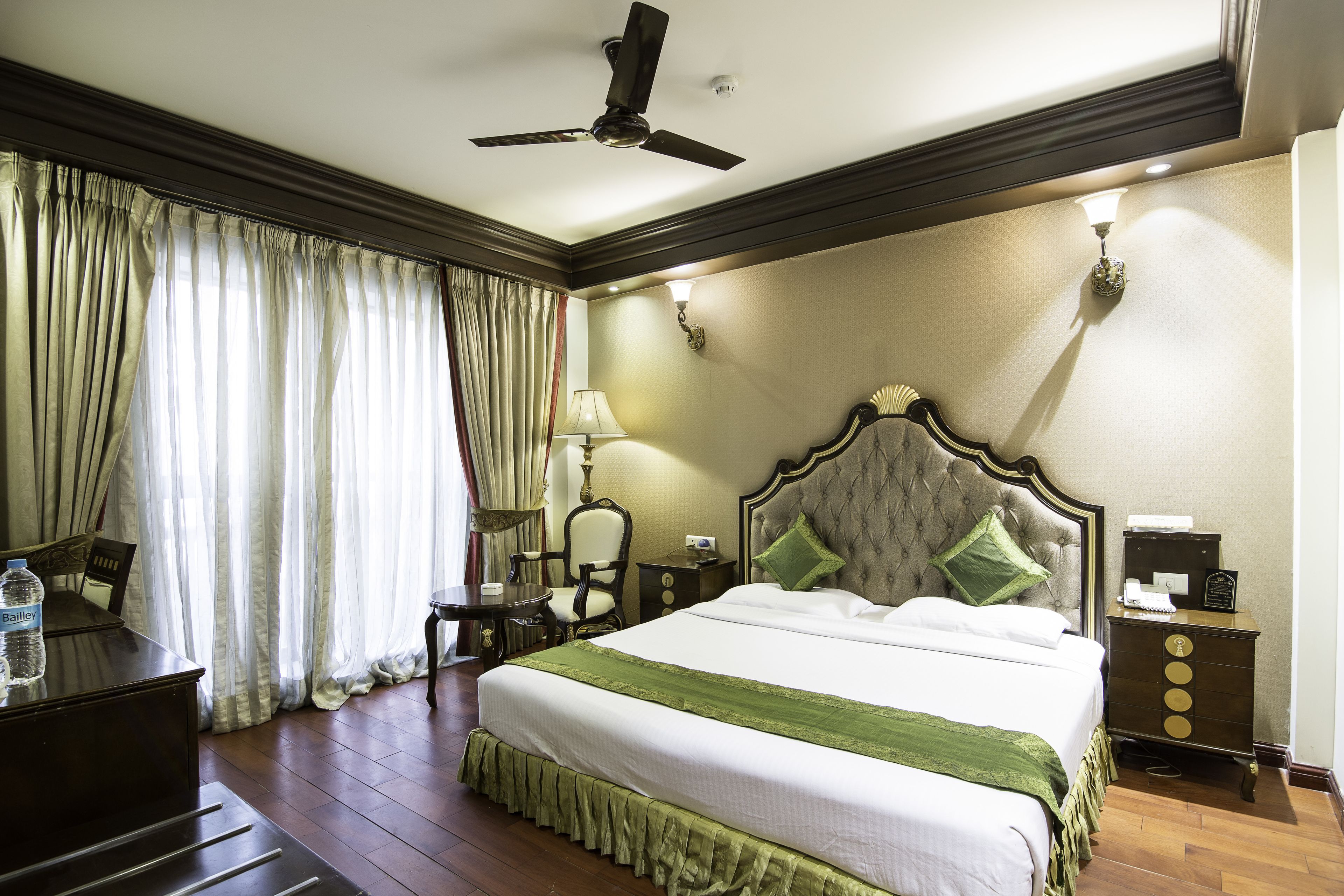 A hotel room with a large bed, a desk, a chair, a nightstand, a lamp, and a ceiling fan.