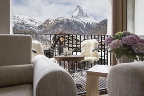 A balcony with a view of snow-capped mountains, a wooden table, and two chairs with white fur throws. - Restaurant - Hotel Sonnmatten (Zermatt)