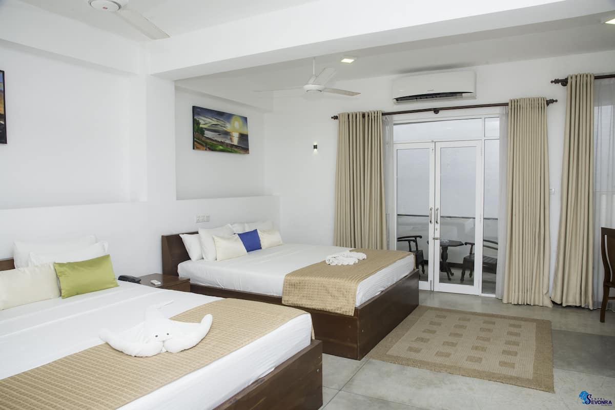 A hotel room with two beds, a ceiling fan, an air conditioning unit, a sliding glass door to the balcony, and a painting on the wall.