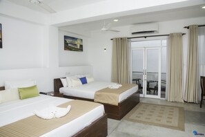 Ein Hotelzimmer mit zwei Betten, einem Deckenventilator, einer Klimaanlage, einer Glastür zum Balkon und einem Gemälde an der Wand.