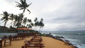 A beach with wooden lounge chairs and a building with a tiled roof. - Sevonra Garden (Unawatuna)