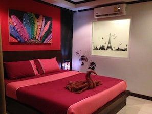 Un letto con biancheria rossa, un quadro astratto dai colori vivaci sopra e una finestra con vista sulla città.
