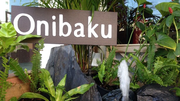 Une pancarte portant l’inscription « Onibaku » se dresse au milieu d’un jardin agrémenté d’une petite cascade, de rochers et de diverses plantes.