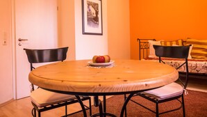 A round wooden table with a plate of apples, two black chairs, a sofa with yellow cushions, and a framed picture on the wall. - Hotel 3 Könige (Aachen)