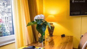 A hotel room with a wooden desk, a laptop, a vase with a white flower, a lamp, and a wall-mounted TV. - Hotel 3 Könige (Aachen)