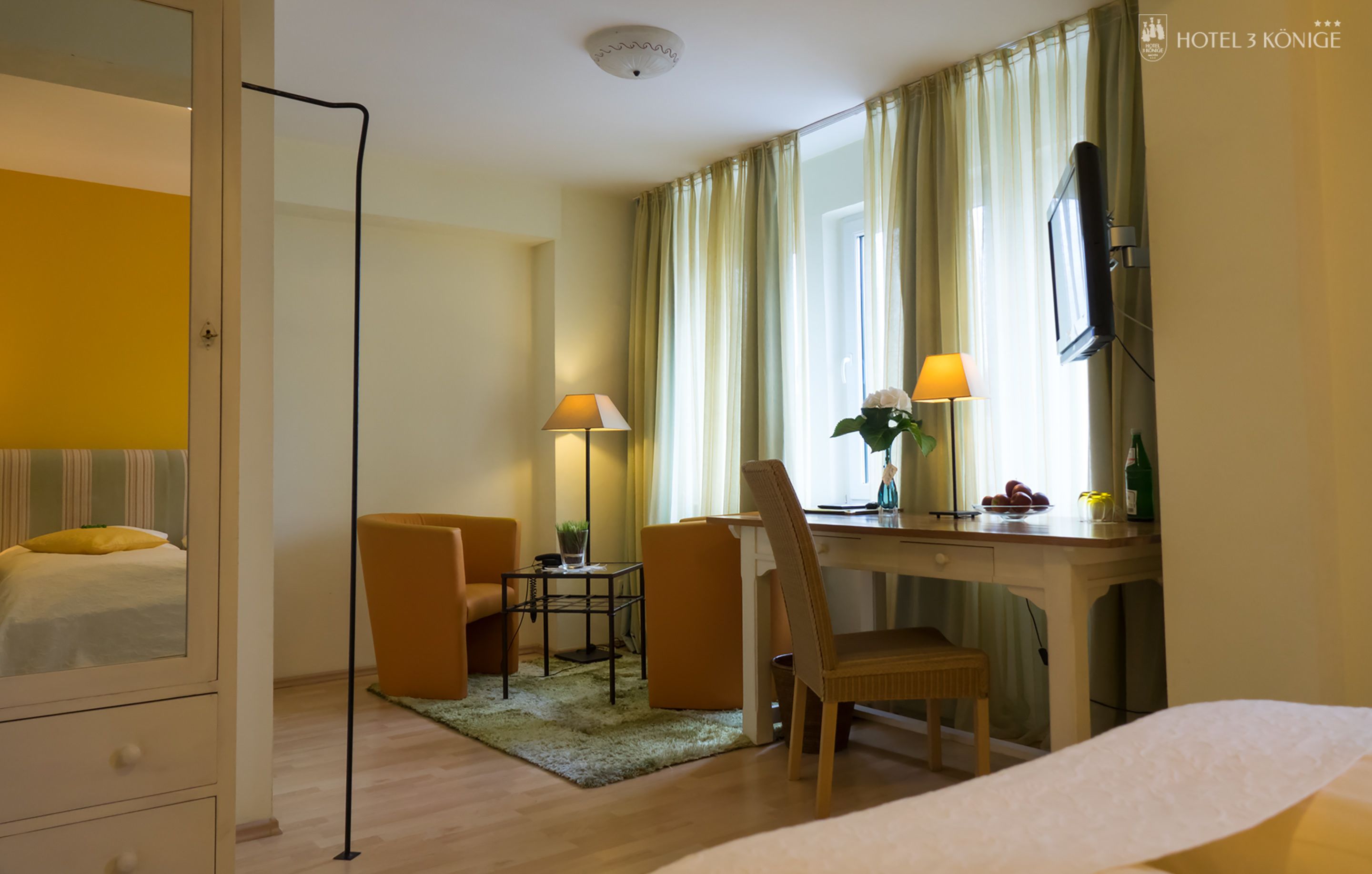 Habitación de hotel con cama, escritorio, silla, televisor y ventana con cortinas.