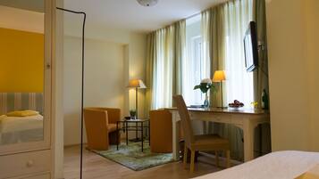 Habitación de hotel con cama, escritorio, silla, televisor y ventana con cortinas.