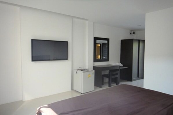 A modern hotel room with a bed, a desk, a chair, a television, and a wardrobe.