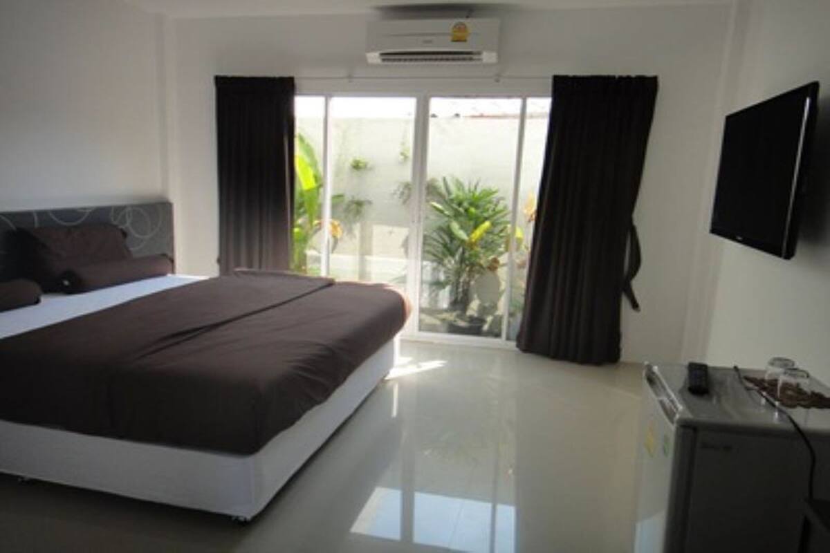 A bedroom with a bed, a television, a small refrigerator, and a sliding glass door to the outside.