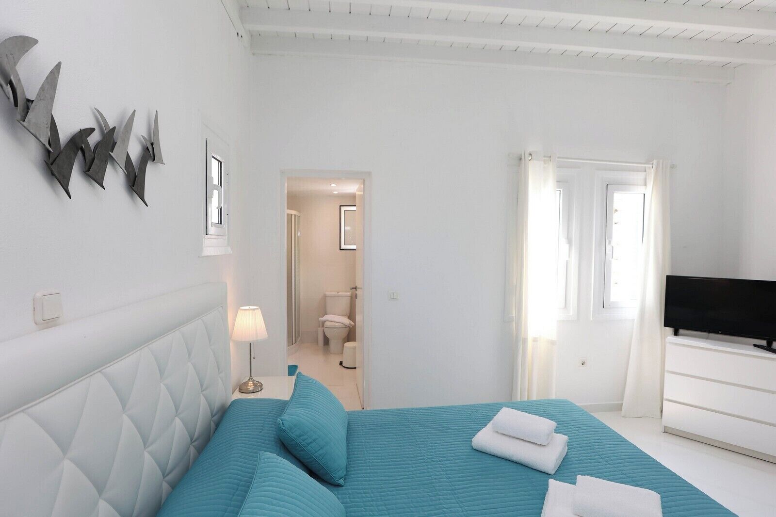 A bedroom with a bed, a TV, and a bathroom visible through an open door.