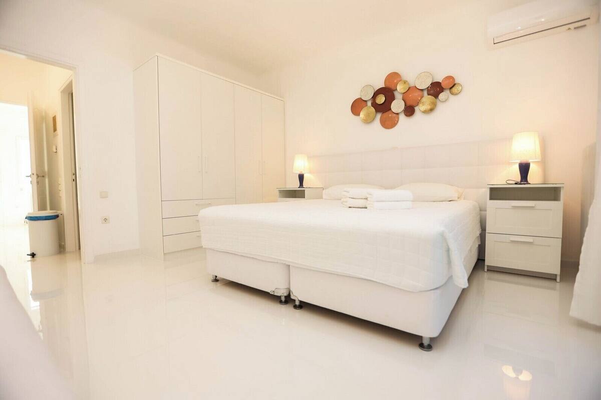 A modern bedroom with a large bed, bedside tables, and a decorative wall piece.