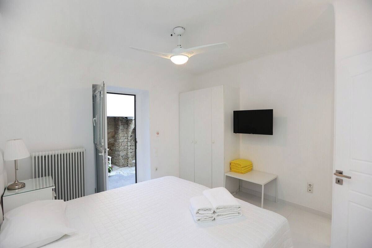 A hotel room with a bed, a bedside table with a lamp, a TV mounted on the wall, and a door leading to an outdoor area.