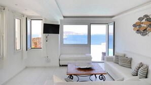 Un salón amplio con un ventanal grande con vistas al mar, un sofá blanco, una mesa de centro y un televisor montado en la pared.