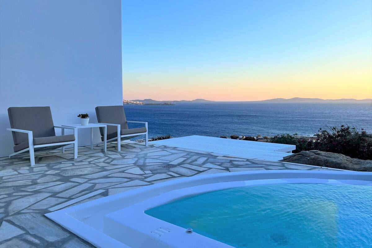 A pool area with a view of the sea, a chair, a small table, and a potted plant.