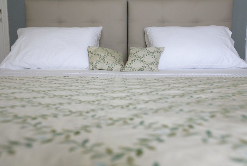 Un lit avec du linge de lit blanc et deux oreillers, dont l’un est orné d’un motif de feuilles.