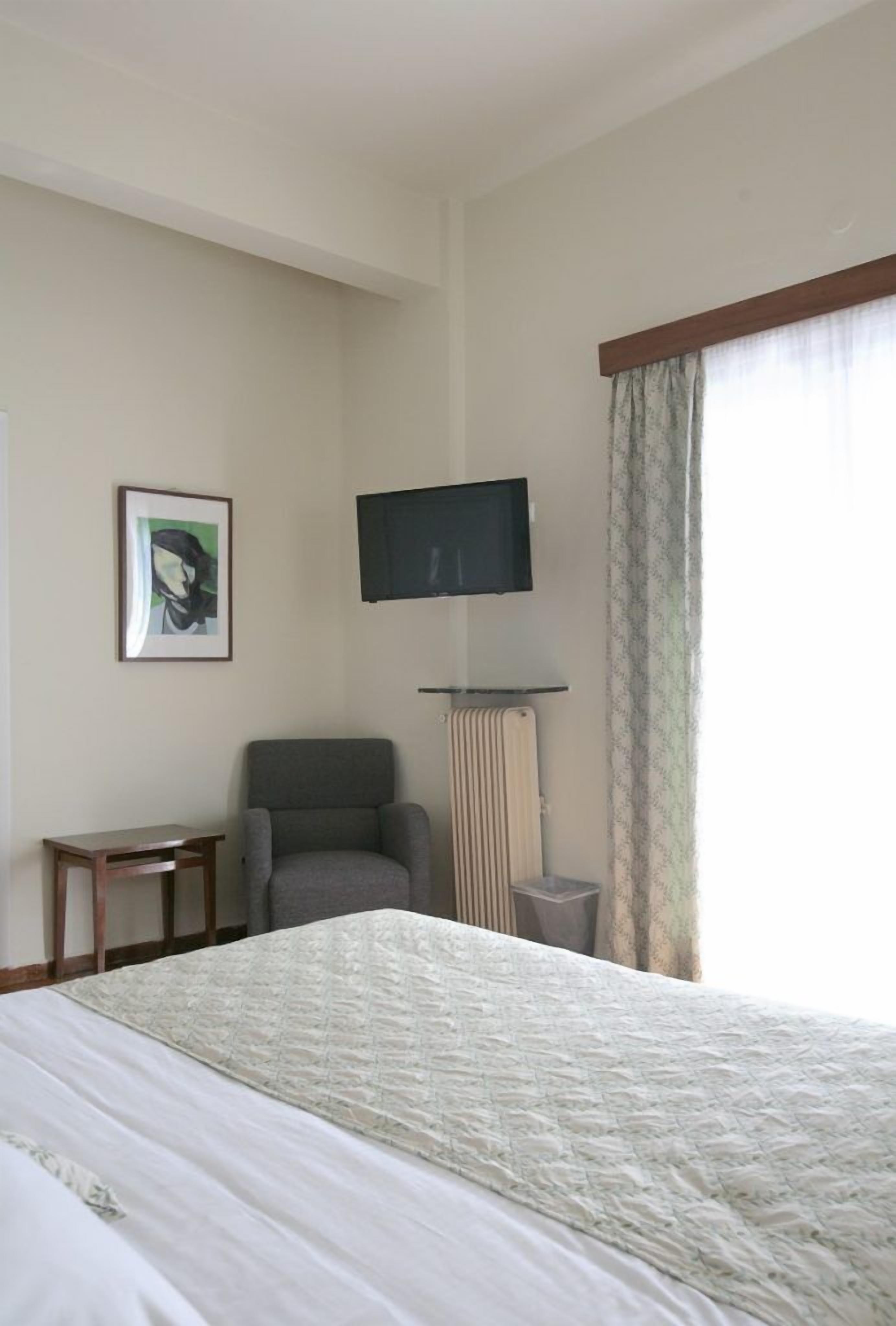 A hotel room with a bed, a chair, a television mounted on the wall, and a window with curtains.
